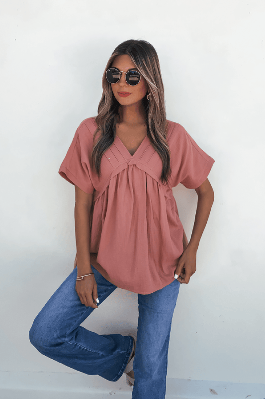 Woman models the Addison Coral Pleated Tunic Top - DOORBUSTER with blue jeans and sunglasses against a plain white background.