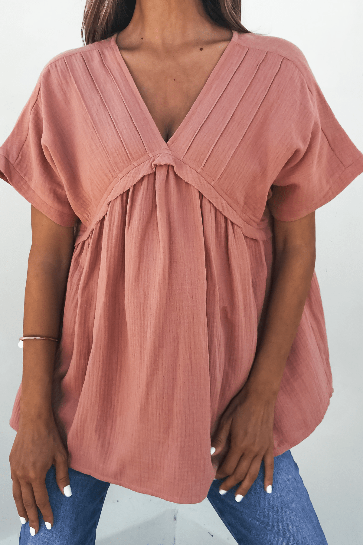 Woman wearing the Addison Coral Pleated Tunic Top – DOORBUSTER, a versatile essential, paired stylishly with blue jeans.