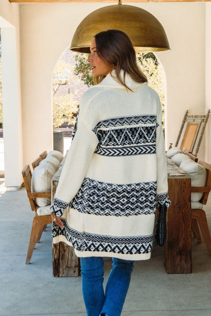 A woman stands outdoors in the Alpine Retreat Ivory and Black Shawl Cardigan, ideal for fall and winter wear.