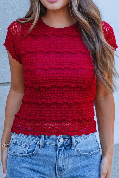 Woman wears the Amara Burgundy High Neck Lace Top with high-waisted blue jeans, perfect for fall, against a light gray wall.