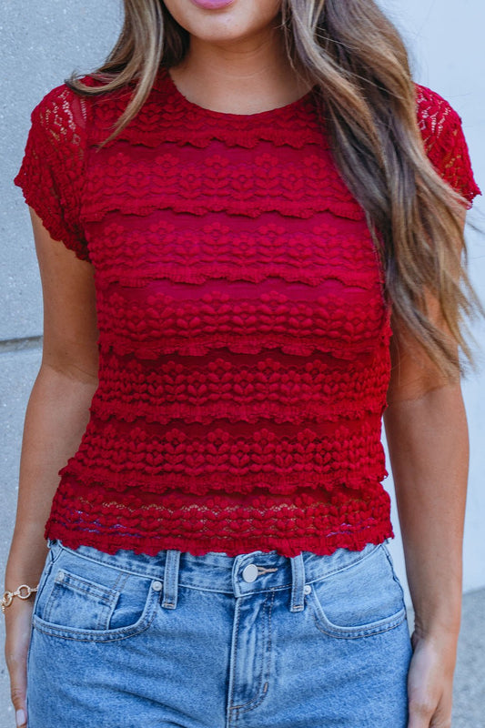 Woman wearing the Amara Burgundy High Neck Lace Top - FINAL SALE with high-waisted blue jeans against a light gray wall.