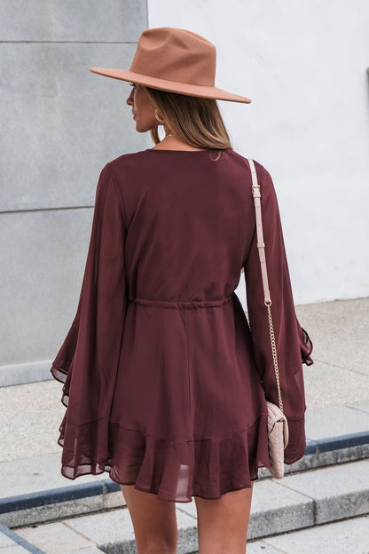 Woman in a brown hat and Amara Ruffled Mini Dress - Brown stands outside, carrying a small beige purse over her shoulder.