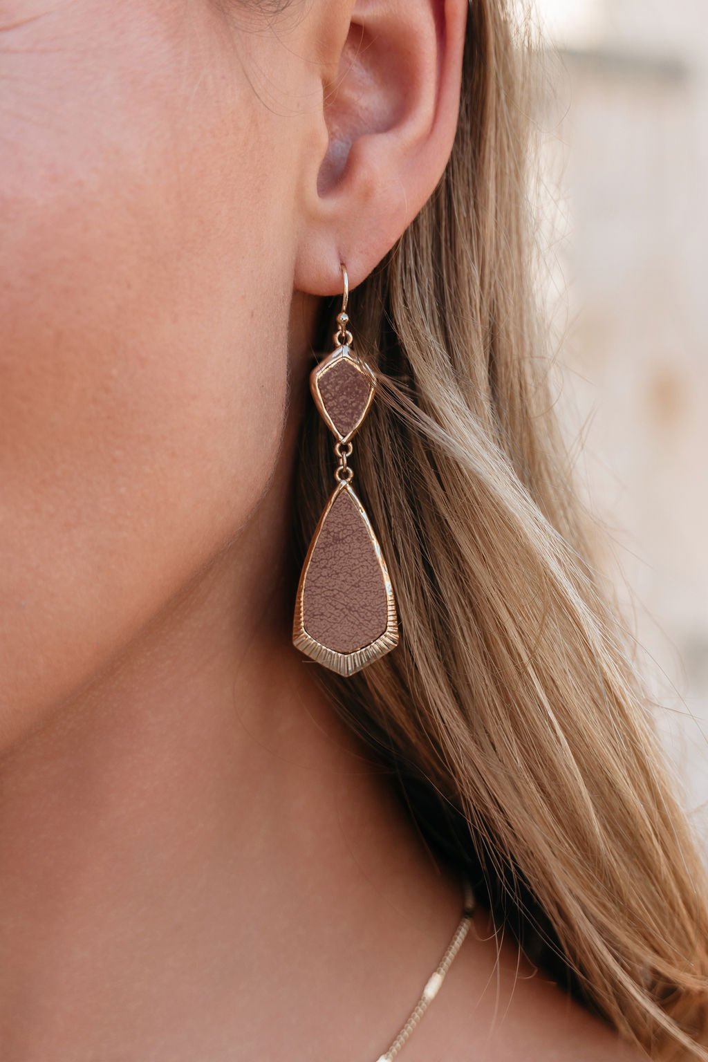 Close-up of a woman's ear wearing Amber Brown Leather Teardrop Earrings with gold frames, and light brown hair visible.