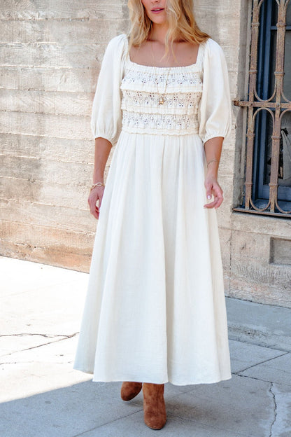 Woman in the Angelica Natural Ruched Midi Dress, standing outdoors by a textured wall, wearing brown boots.