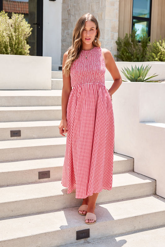 Woman wearing the Gingham Open Back Maxi Dress - Red, standing on outdoor steps by a modern building.