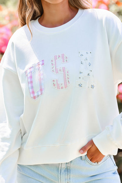 A woman wears the Bold & Free Patchwork Sweatshirt in white with light blue jeans outdoors.