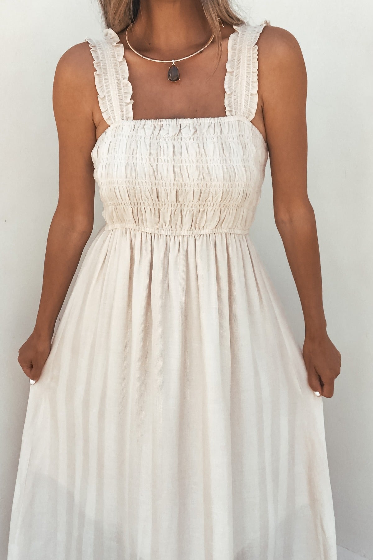 Woman wearing the Arwen Ruffle Smocked Midi Dress - Natural, holding the skirt against a plain background.