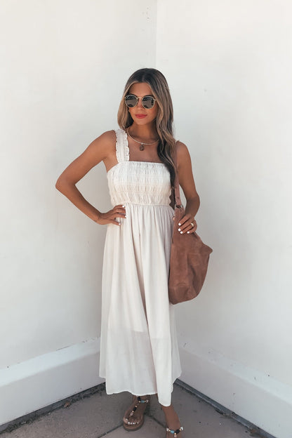 Woman in the Arwen Ruffle Smocked Midi Dress - Natural, with ruffled straps, carrying a brown tote and wearing sunglasses.