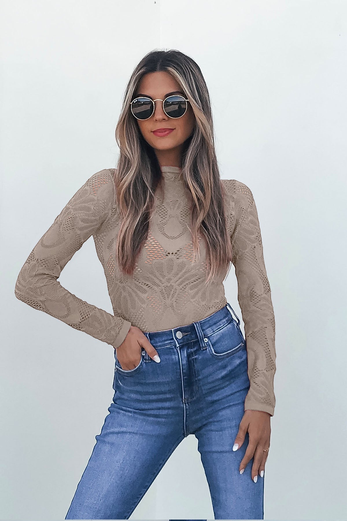 Woman in Ash Mauve Mock Neck Fishnet Top and high-waisted blue jeans poses against a plain light background.