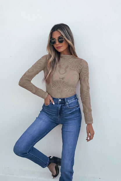 Woman wearing sunglasses, Ash Mauve Mock Neck Fishnet Top, and high-waisted jeans poses against a white wall with one hand in pocket.