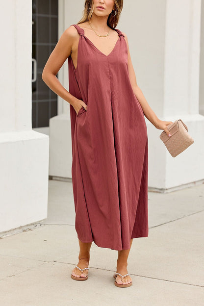 Woman wears the Audrey Knot Strap Midi Dress in burgundy, holding a beige purse and wearing sandals.