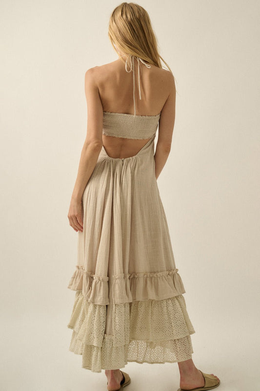 A woman with long blonde hair models the Aurora Natural Mixed Lace Maxi Dress, with a halter neckline and lace ruffle details, back view.