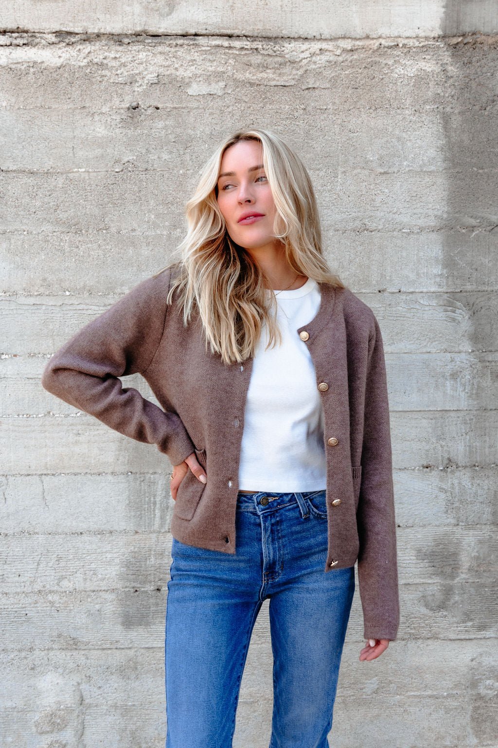 A woman with long blonde hair wears the Autumn Button Front Sweater Cardigan in brown, a white shirt, and blue jeans.