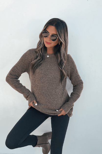 Woman in sunglasses poses against a white wall, wearing the Autumn Glow Brushed Ochre Waffle Knit Sweater, black pants, and brown boots.