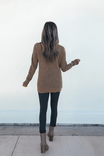 A woman with long hair wears the Autumn Glow Brushed Ochre Waffle Knit Sweater, black pants, and brown boots, facing away.