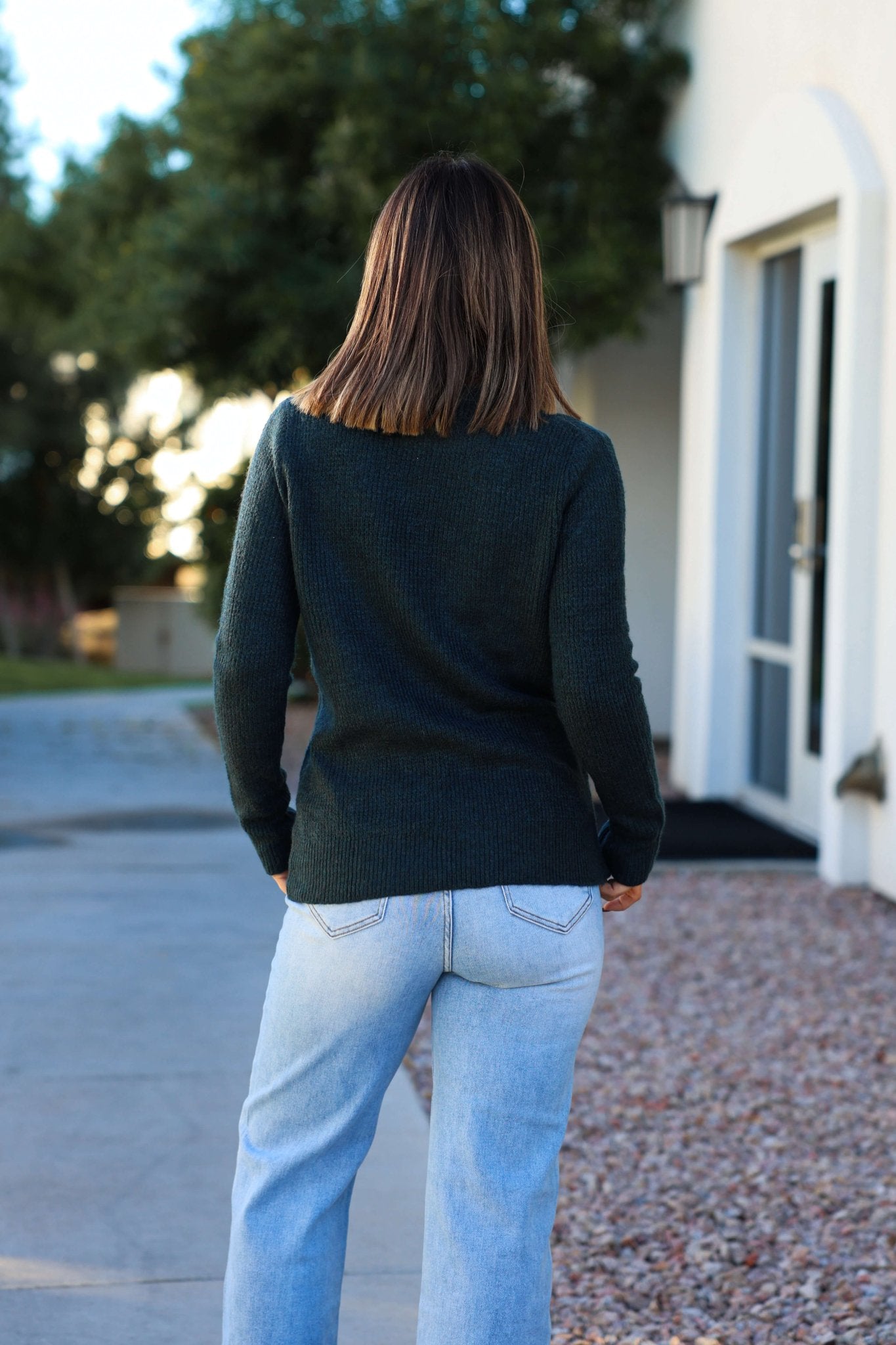 A woman in the Autumn Glow Brushed Teal Waffle Knit Sweater and light jeans stands outside, facing away from the camera.