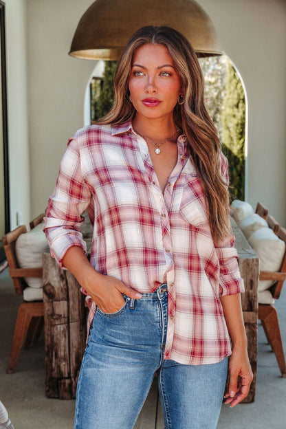A woman in an Autumn Spice Wine Plaid Shirt and jeans stands outdoors with one hand in her pocket, looking to the side.