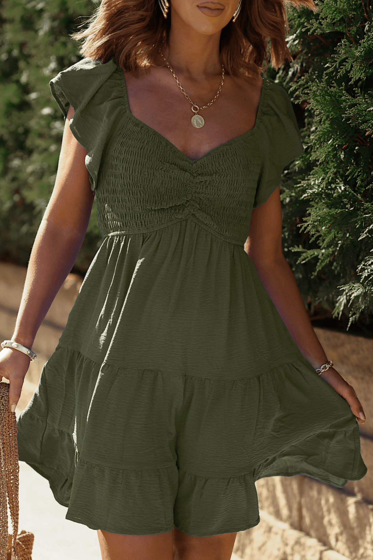 Woman wearing Ava's Sweetheart Olive Mini Dress with a smocked bust, tiered skirt, and gold necklace outdoors.