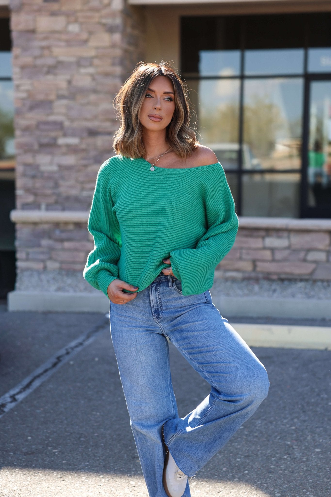 Woman outdoors in front of a stone building wears the Avery Ribbed Boat Neck Sweater in green and blue jeans.