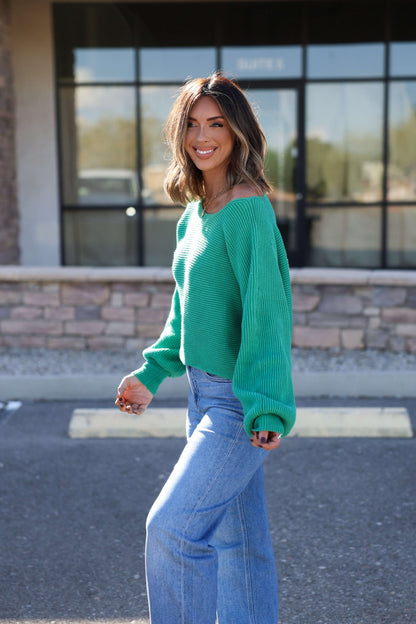 Woman wearing the Avery Ribbed Boat Neck Sweater in green stands outdoors, smiling at the camera.