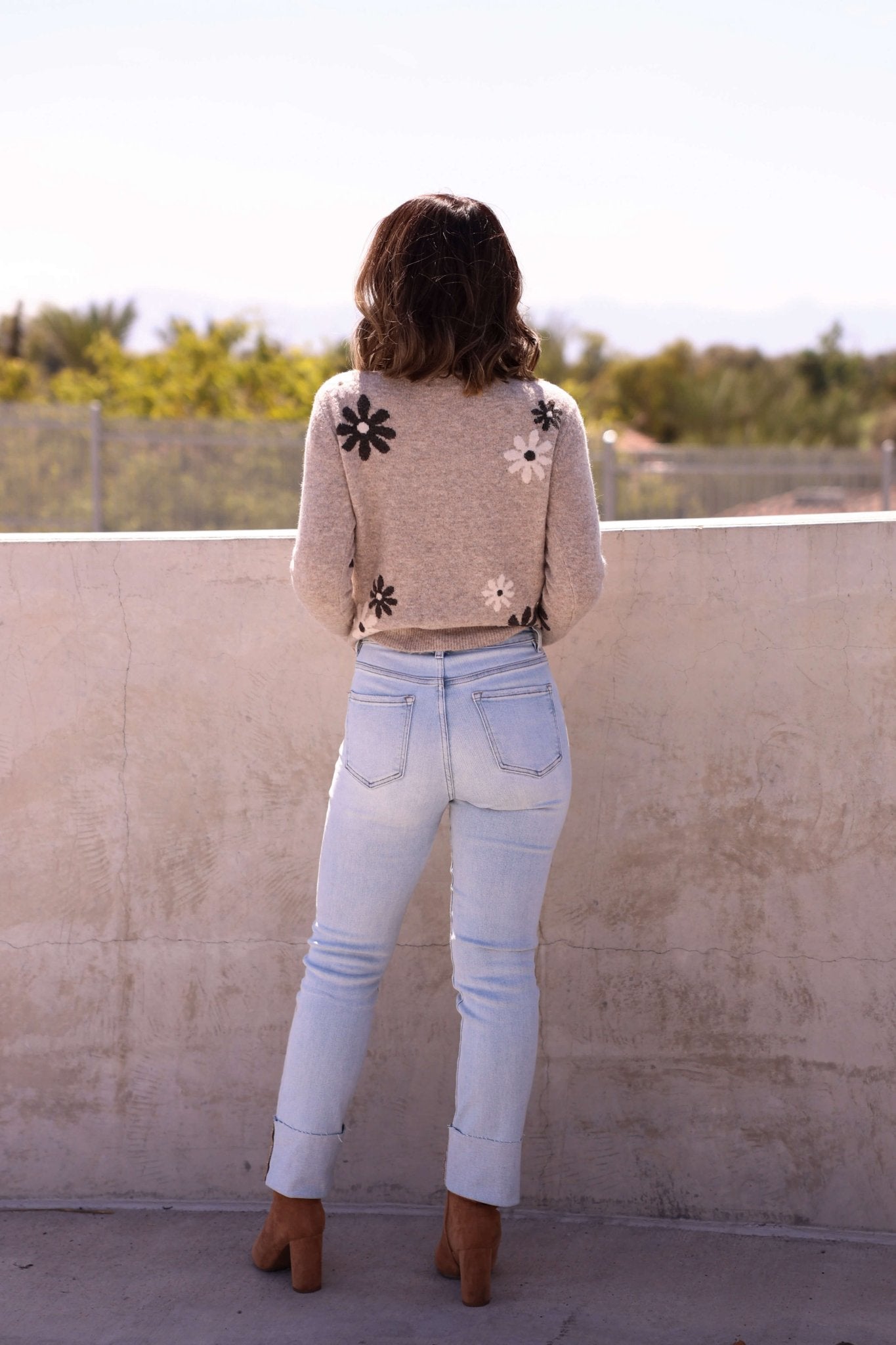 A woman with wavy hair wears Bayeas Light Blue Straight Leg Cuffed Jeans—Final Sale—while standing outdoors, back to camera.