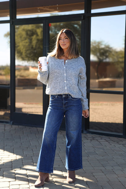 Woman in a gray sweater and Bayeas Lisa Dark Wash Wide Leg Jeans holds a coffee cup outside a building with glass windows.