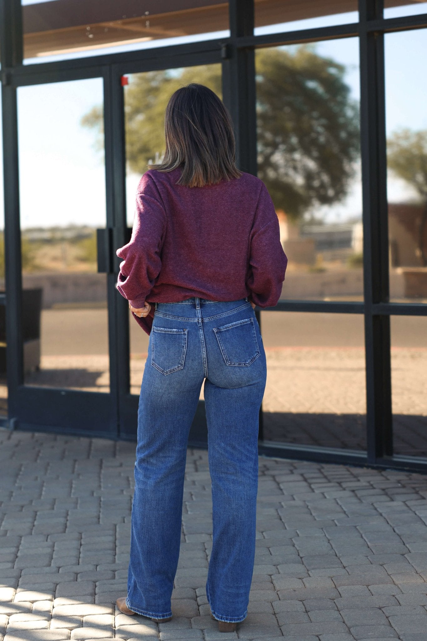 A woman in Bayeas Medium Wash Relaxed Straight Leg Jeans stands outside, facing away from glass doors on a paved walkway.