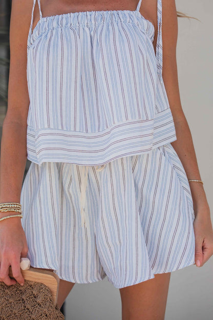 Woman in a blue Bayview Stripe Tie-Strap Top and shorts set, holding a woven bag and wearing bracelets.