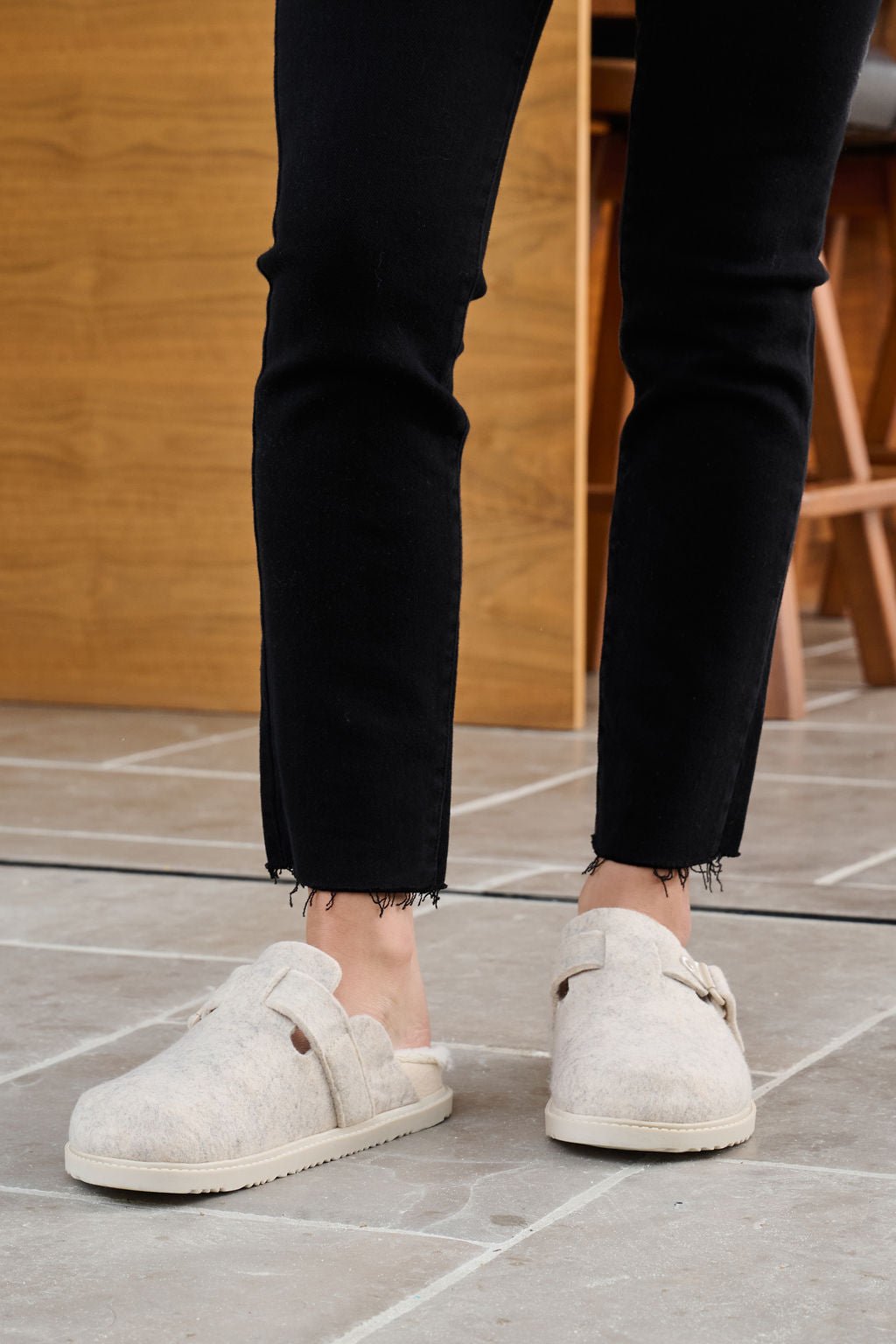 Someone in Beach By Matisse Portland Oatmeal Brushed Clogs and black pants stands on a tiled floor with wooden furniture behind.