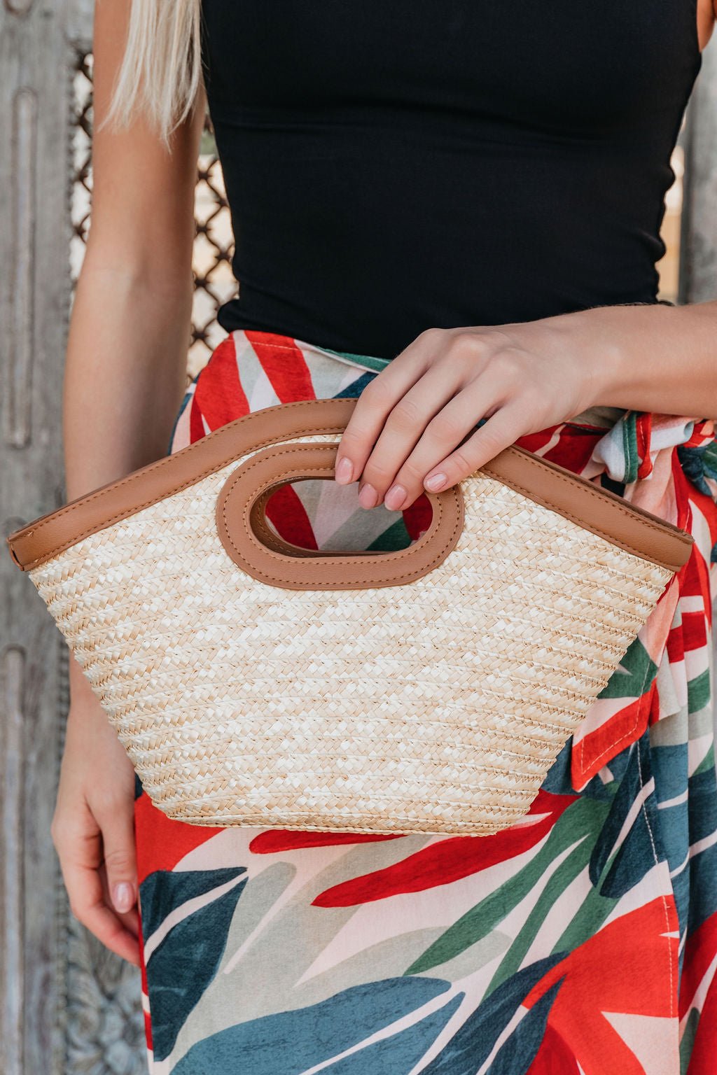 A woman in a black top and colorful skirt holds the Beachwood Bliss Bucket Bag with brown leather handles and straw texture.