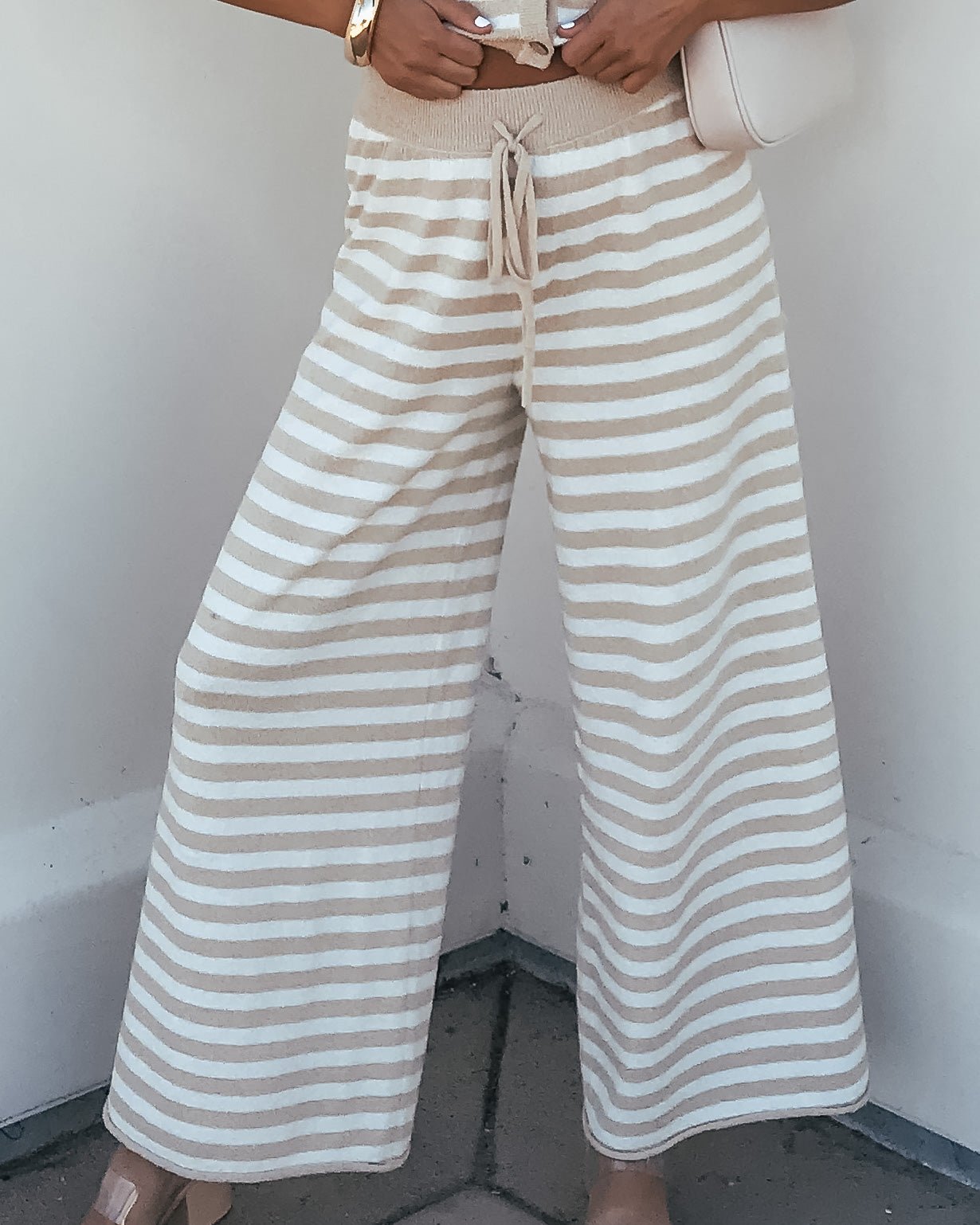 Woman wearing Beige and Ivory Striped Lounge Pants | Pre Order, holding a light purse, lower body visible.