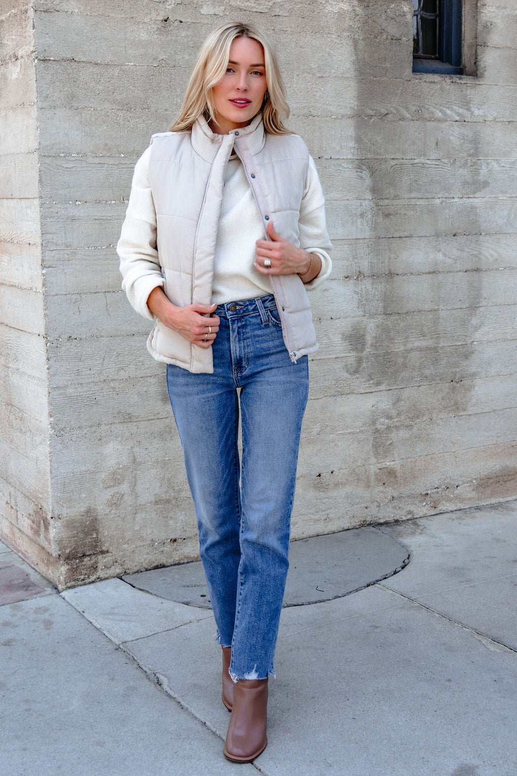 Woman in a Beige Button Up Puffer Vest, white sweater, blue jeans, and brown boots—perfect layering for fall.