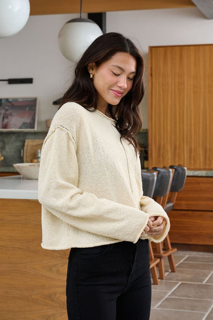 A woman in a Beige Contrast Stitch Detail Sweater and black pants smiles with eyes closed in a modern kitchen.