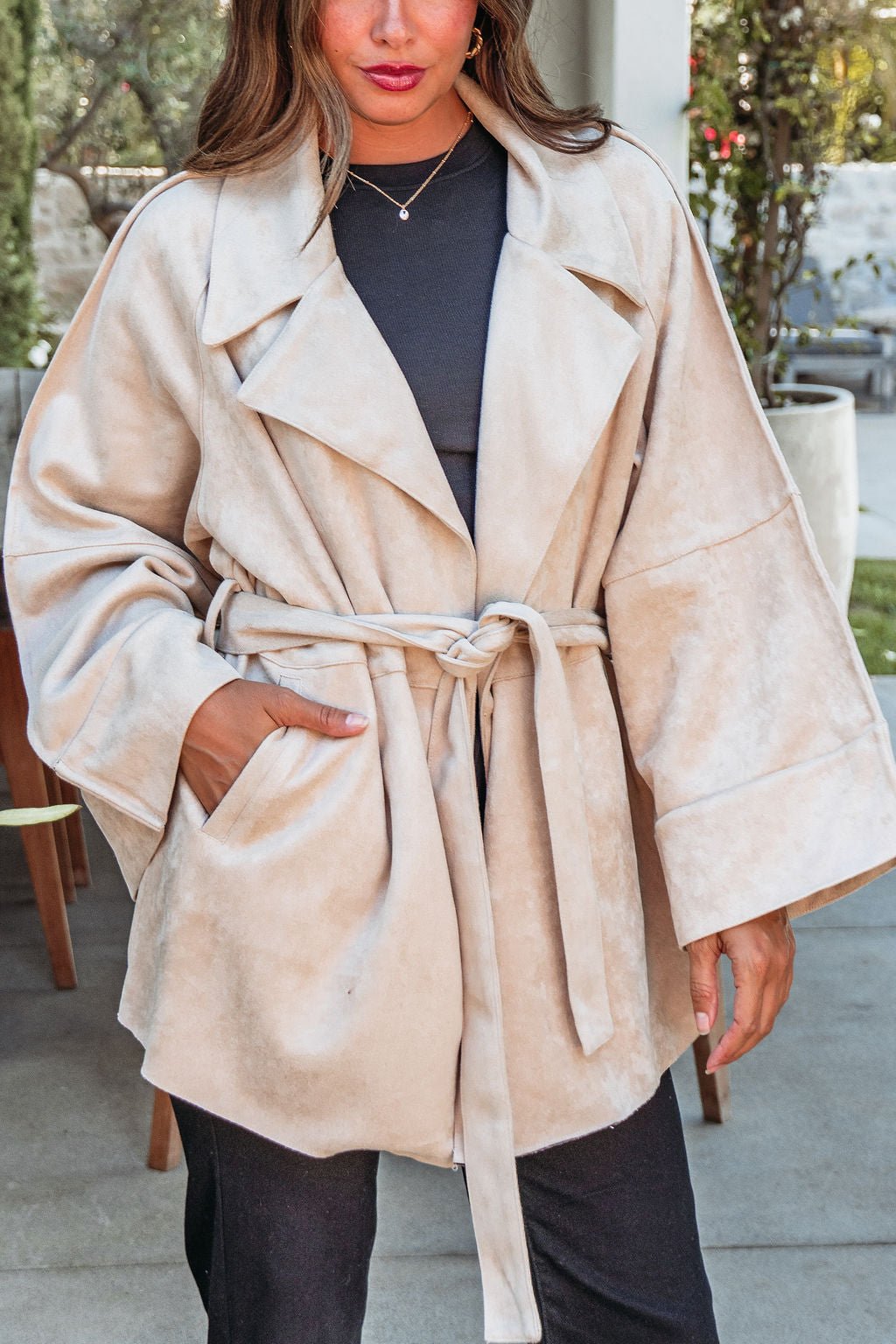 A woman models the Beige Faux Suede Belted Coat - FINAL SALE outdoors, pairing it with a black outfit for chic fall style.