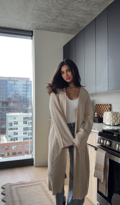 A woman models the Beige Ribbed Open Front Duster Cardigan - FINAL SALE in a modern kitchen with city views, perfect for winter layering.
