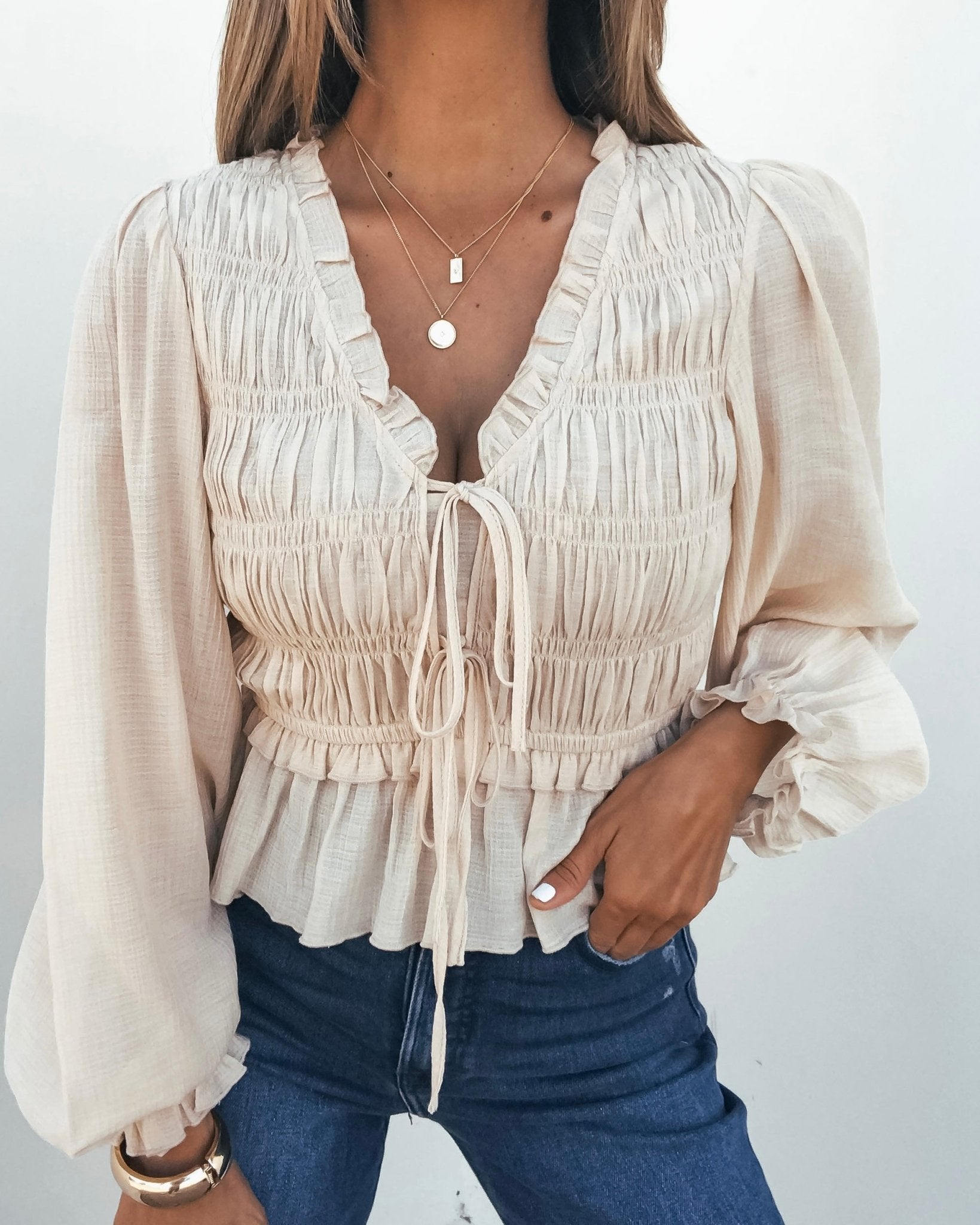 Woman in a Beige Ruffle Smocked Peplum Top, blue jeans, and layered necklaces.