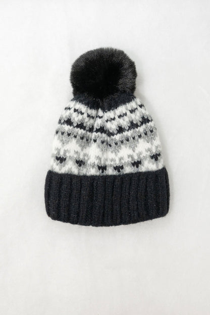 The Black Aztec Pom Beanie features a dark pom-pom, black and white pattern, and thick ribbed brim on a white background.