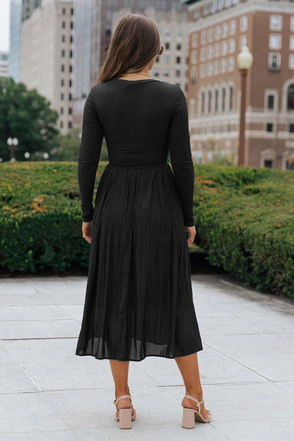 A woman models the Black Contrast Pleated Midi Dress outdoors, facing away from the camera in beige heels.