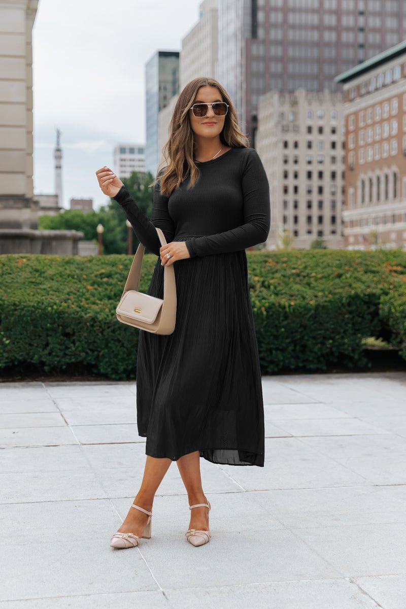 A woman wears the Black Contrast Pleated Midi Dress, featuring elegant ribbed details.