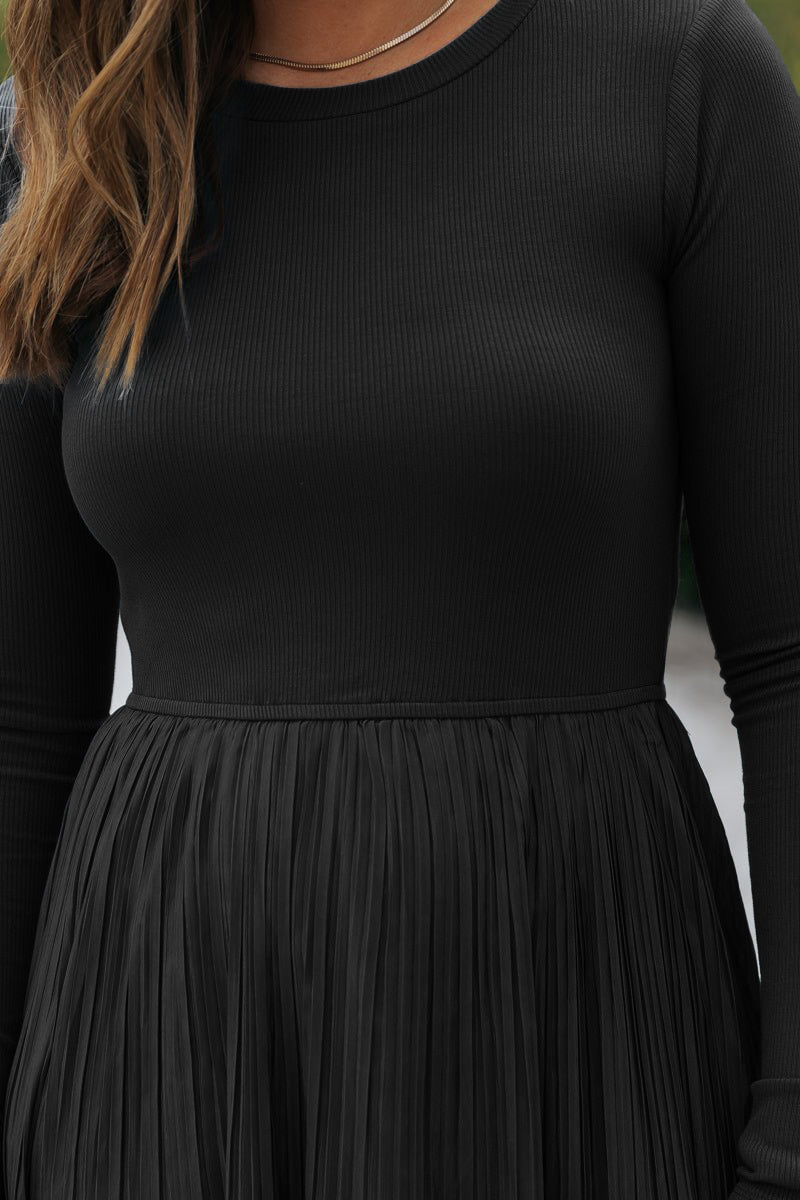 Wearing a Black Contrast Pleated Midi Dress, featuring ribbed details and a pleated skirt. Face not visible.