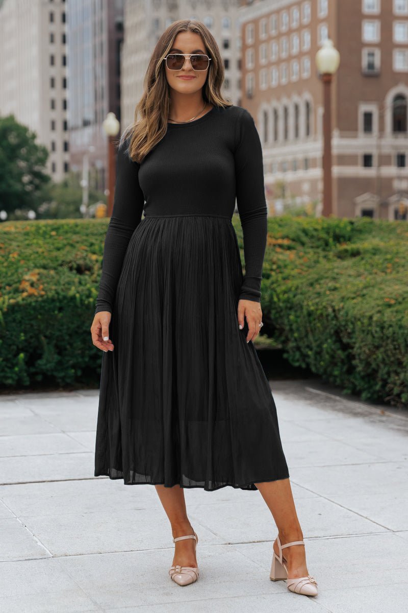 A woman in sunglasses wears the Black Contrast Pleated Midi Dress with beige heels, standing on a city sidewalk.