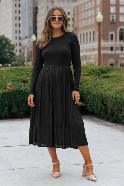 A woman in sunglasses wears the Black Contrast Pleated Midi Dress with beige heels, standing on a city sidewalk.