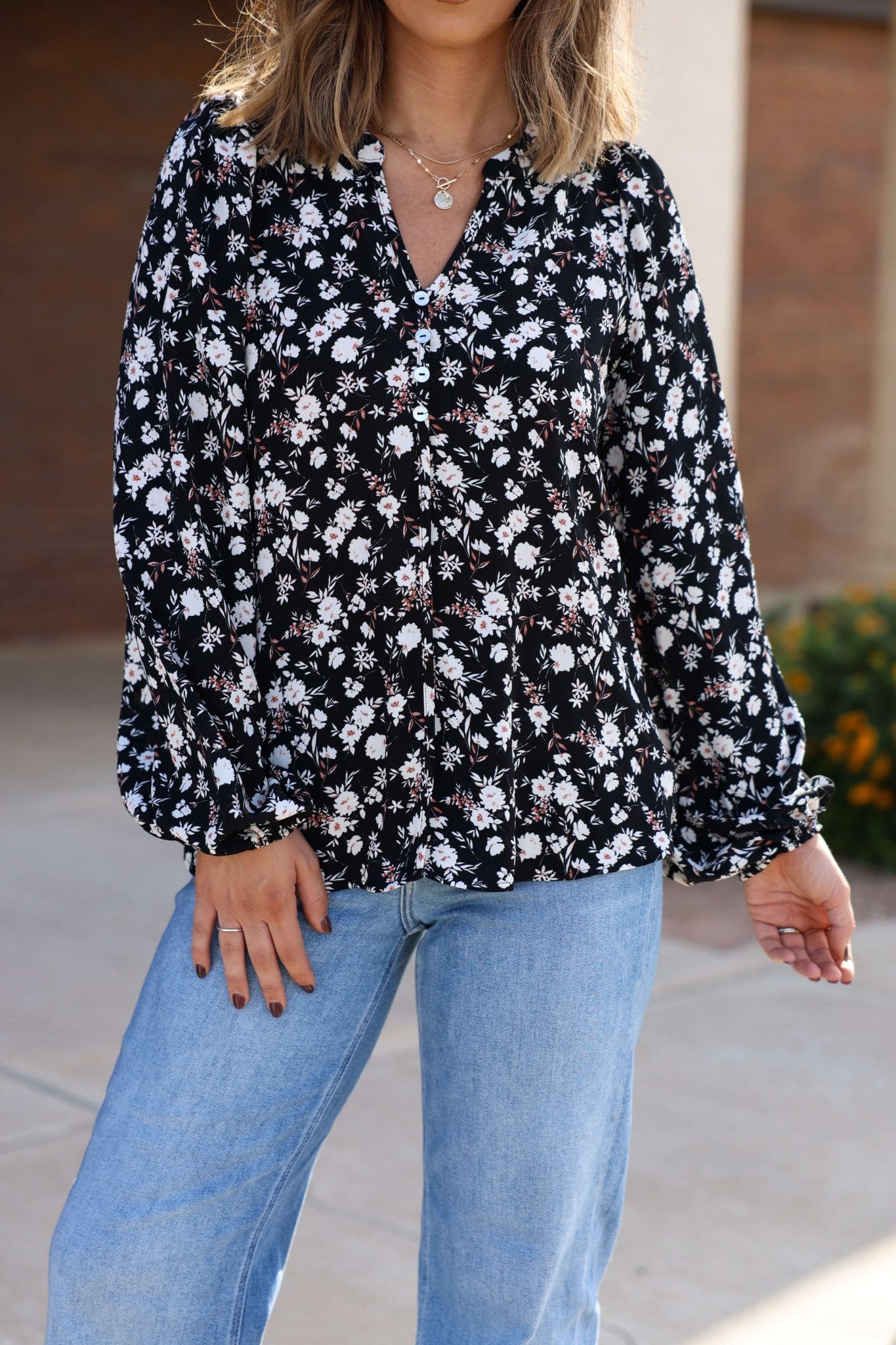 Woman in the Black Floral Button Down Blouse - FINAL SALE, paired with light blue jeans, poses outdoors.
