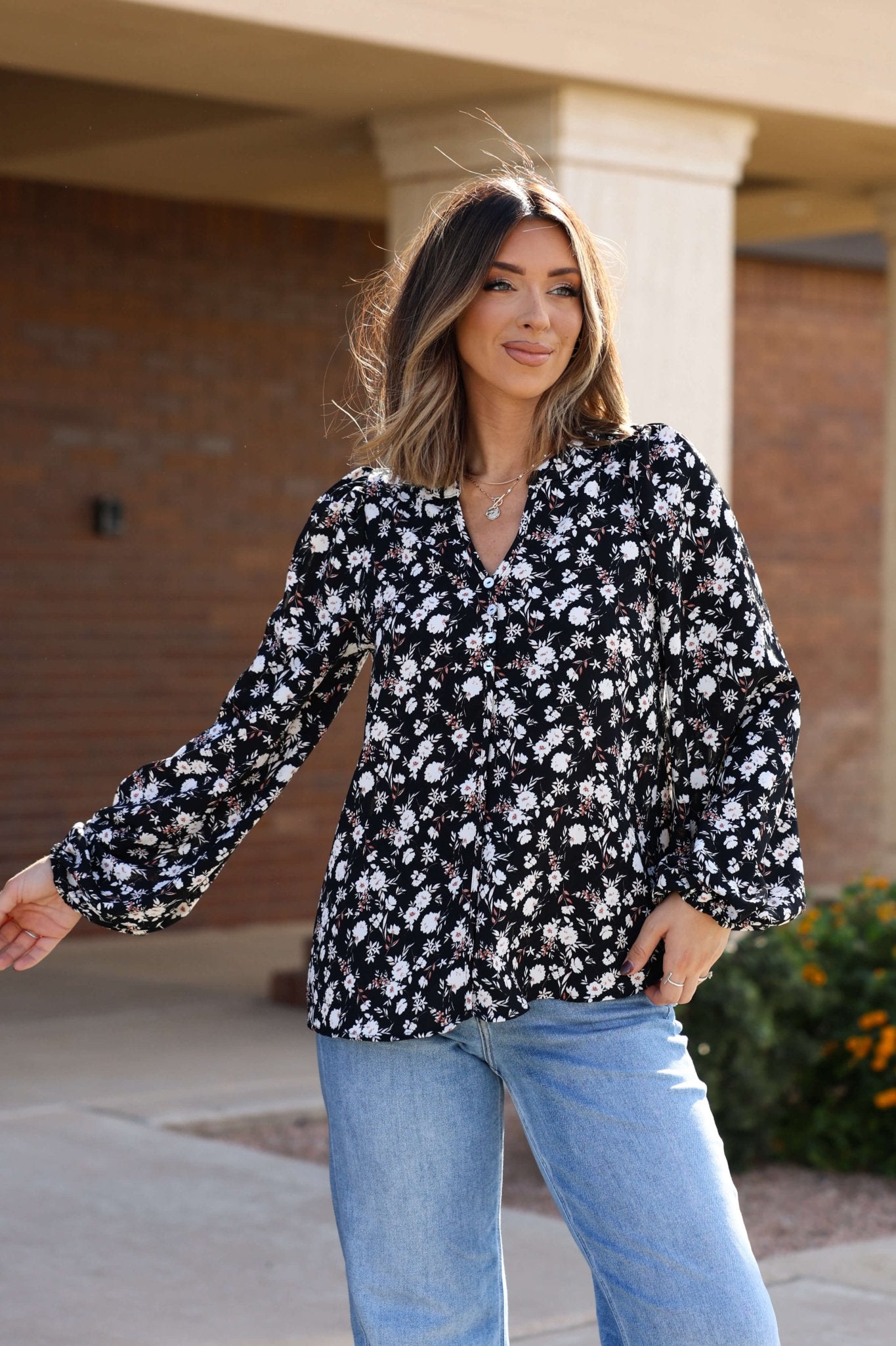 Woman wearing the Black Floral Button Down Blouse - FINAL SALE and light blue jeans, smiling outdoors.