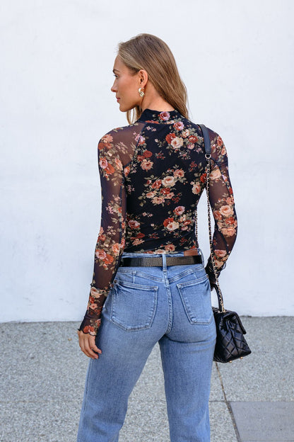 Woman facing away in the Black Floral Mesh Long Sleeve Top, light blue jeans, and a black quilted purse.