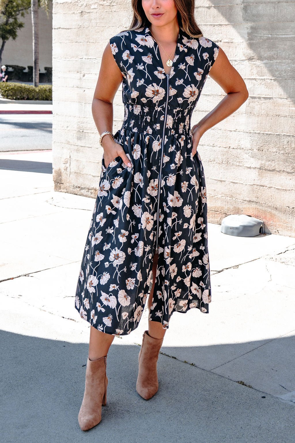 Woman in a Black Floral Print Smock Zip Midi Dress with pockets and tan ankle boots, standing outdoors.