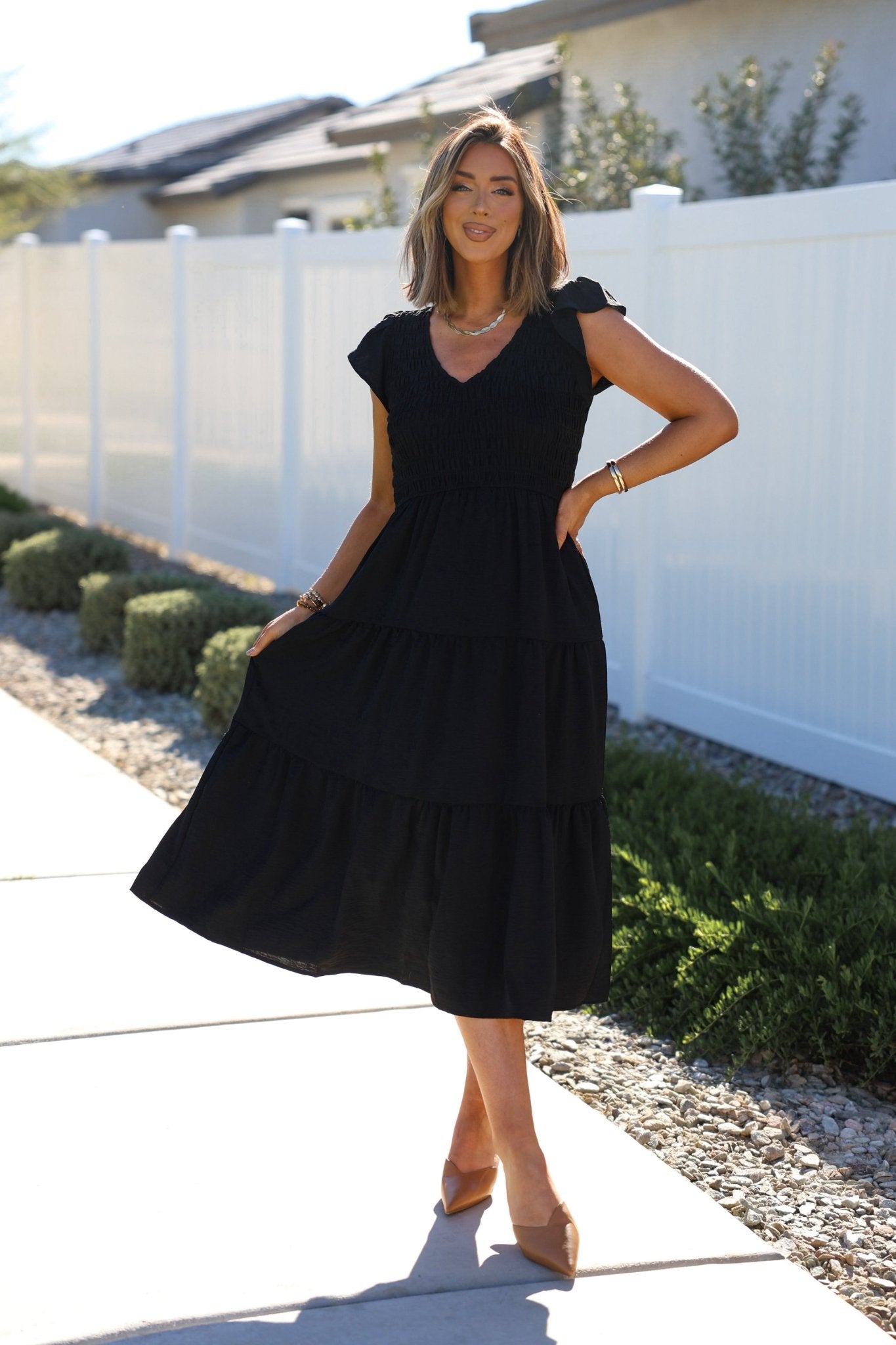 Woman wearing a black flutter sleeve midi dress outdoors.