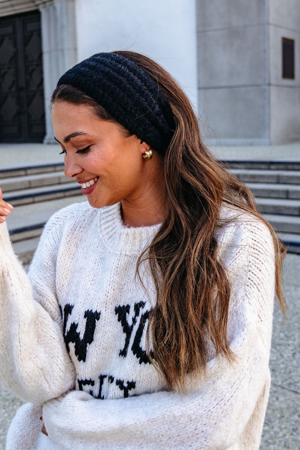 Woman with long hair in a white sweater wears a Black Fuzzy Soft Cable Knit Headband while standing outdoors near steps.