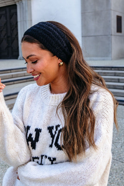 Woman with long hair in a white sweater wears a Black Fuzzy Soft Cable Knit Headband while standing outdoors near steps.
