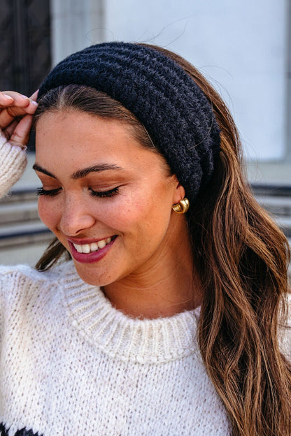 Smiling woman with long brown hair wears a white sweater, gold hoops, and a Black Fuzzy Soft Cable Knit Headband.